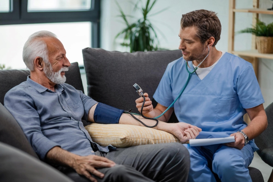 happy-general-practitioner-measuring-blood-pressure-mature-man-while-being-home-visit