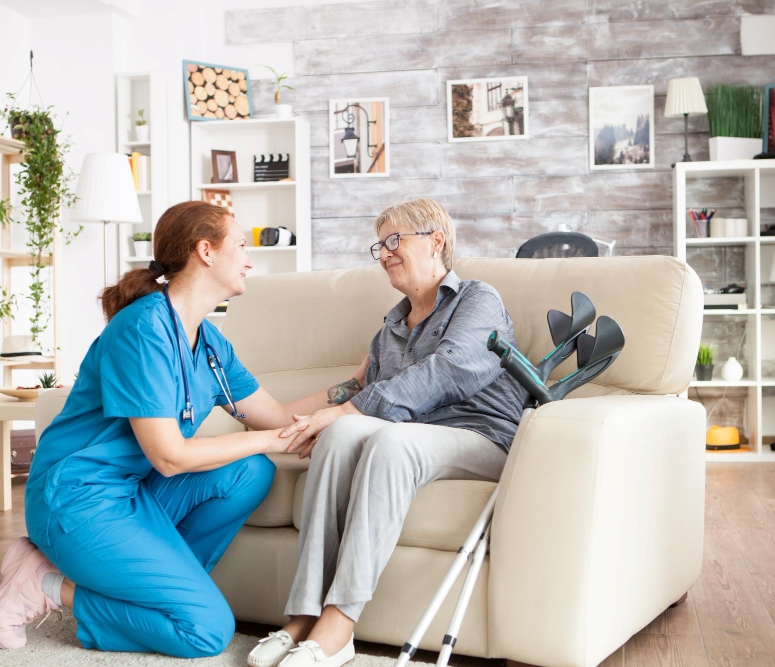 joyful-old-lady-sitting-couch-nursing-home-holding-health-taker-arm