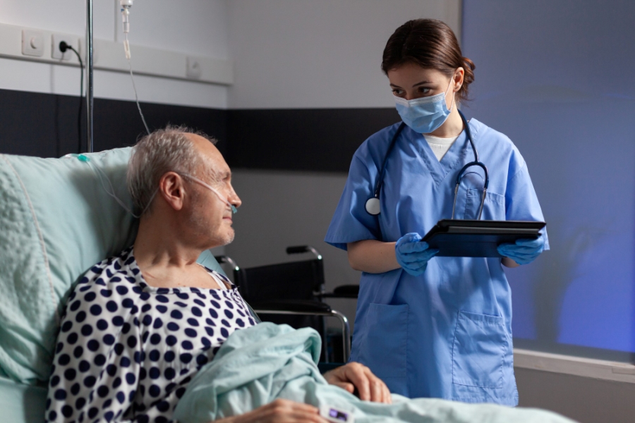 medical-assistant-with-protection-mask-checking-treatment-senior-man-reading-notes-tablet-pc